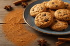 Cookies on a plate with cinnamon powder and sticks on a wooden surface