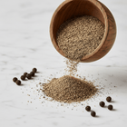 Black pepper table grind in a rustic wooden bowl with whole peppercorns on white marble