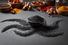 Black sesame seeds on dark slate surface with ceramic bowl