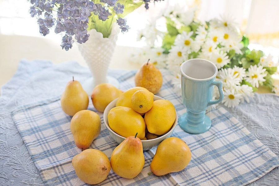 a bowl of pears on a table cloth surrounded by flowers and reacup